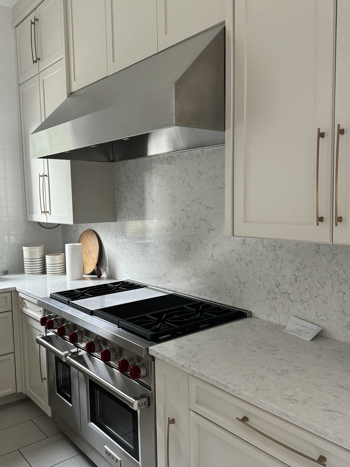 Kitchen after renovation with light cabinetry, stone backsplash and Wolf range